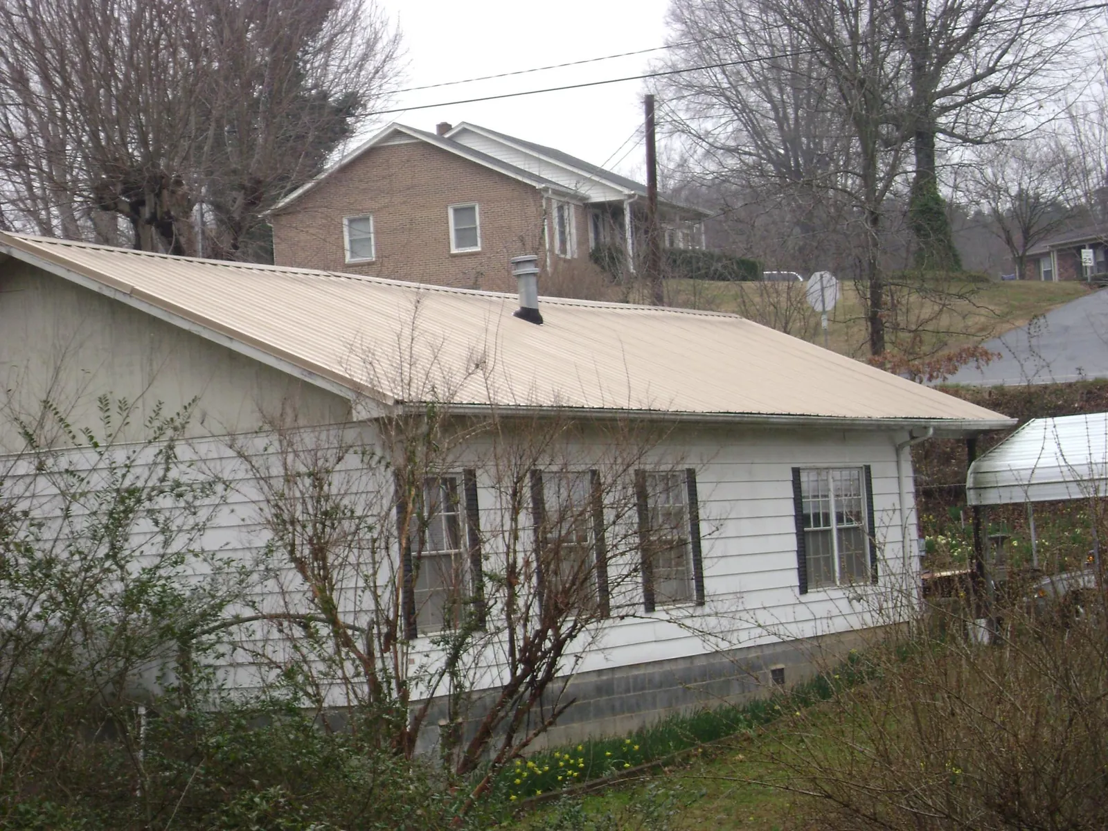 Tan metal roof on a white sided house set into a hillside — Commercial Roofing by Roofing Brothers in Memphis